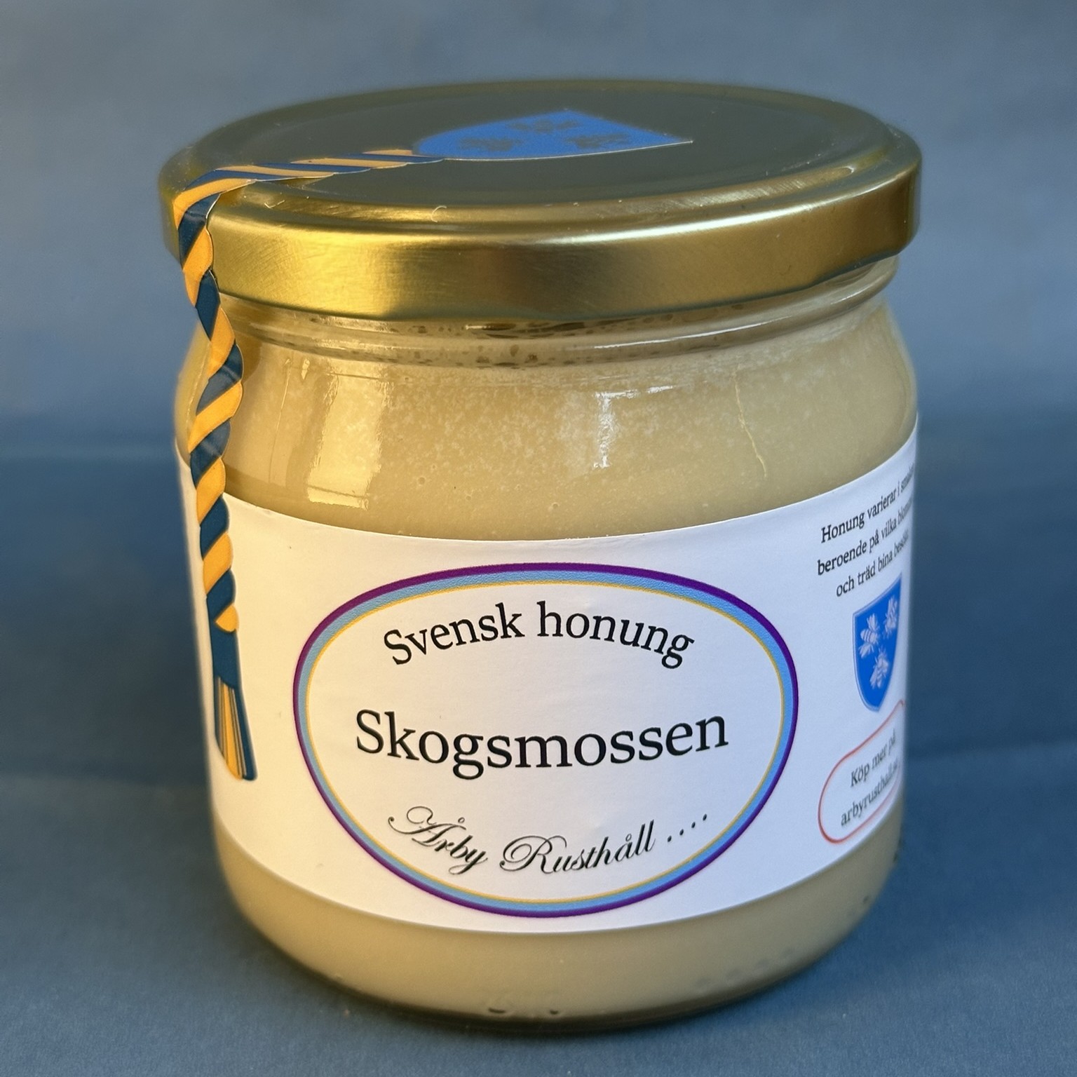 Glasburk med honung. Texten "Skogsmossen" står i en blålila oval.